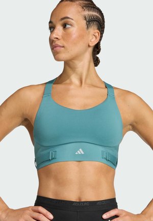 Tirkizni sportski grudnjak s širokim trakama i podesivim kopčama. Ima glatku, rastezljivu tkaninu i adidas logotip sprijeda. Vidljiv crni pojas.