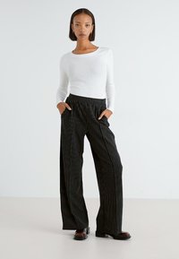 Black striped wide-leg pants with a high waistband, featuring side pockets, paired with a fitted white long-sleeve top. Smooth texture.