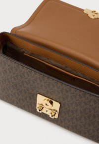 Καφέ δομημένη τσάντα χειρός με υφή στην εξωτερική επιφάνεια, χρυσά μεταλλικά κλεισίματα και εσωτερική επένδυση από λείο ύφασμα. Διαθέτει πάνω καπάκι και άφθονο χώρο.