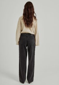 Jeans negros de pierna ancha con una cintura alta, que cuentan con dos bolsillos traseros y una sutil textura deslavada, combinados con un suéter de punto beige.