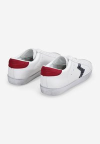White leather sneakers with red accents at the heel, a sparkly black side logo, and a textured grey rubber sole. Laced design.