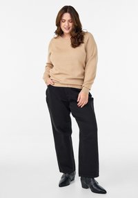 Maglione beige con texture e scollatura rotonda, abbinato a pantaloni neri larghi e scarpe nere con dettagli decorativi.