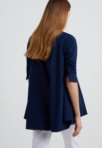 Mörkblå blus med lös passform, med gathers detaljer vid ärmarna och en hög-låg nederkant, tillverkad av ett mjukt tyg.