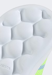 Sole of a sneaker featuring a textured white rubber surface with rounded elements for grip; bright green knit upper with blue accents.