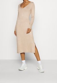 Robe beige en maille avec manches longues, encolure en V et fente latérale, associée à des chaussures de sport mint clair et des chaussettes blanches.