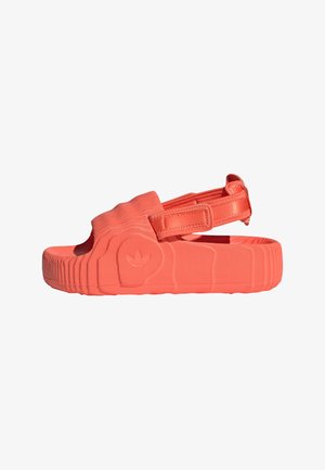 Coral rubber sandal with an adjustable strap, textured surface, open toe design, and a patterned sole featuring a brand emblem.