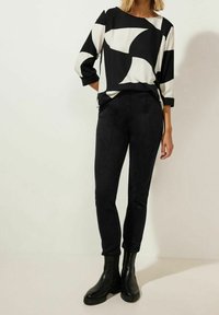 Top geometrico in bianco e nero con maniche a tre quarti, abbinato a pantaloni neri aderenti e stivaletti neri chunky.