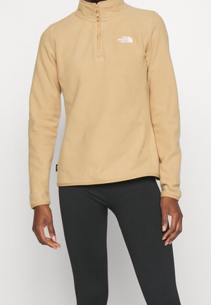 Beżowy polar z suwakiem do ćwiartki i logo The North Face na piersi, noszony z czarnymi legginsami.