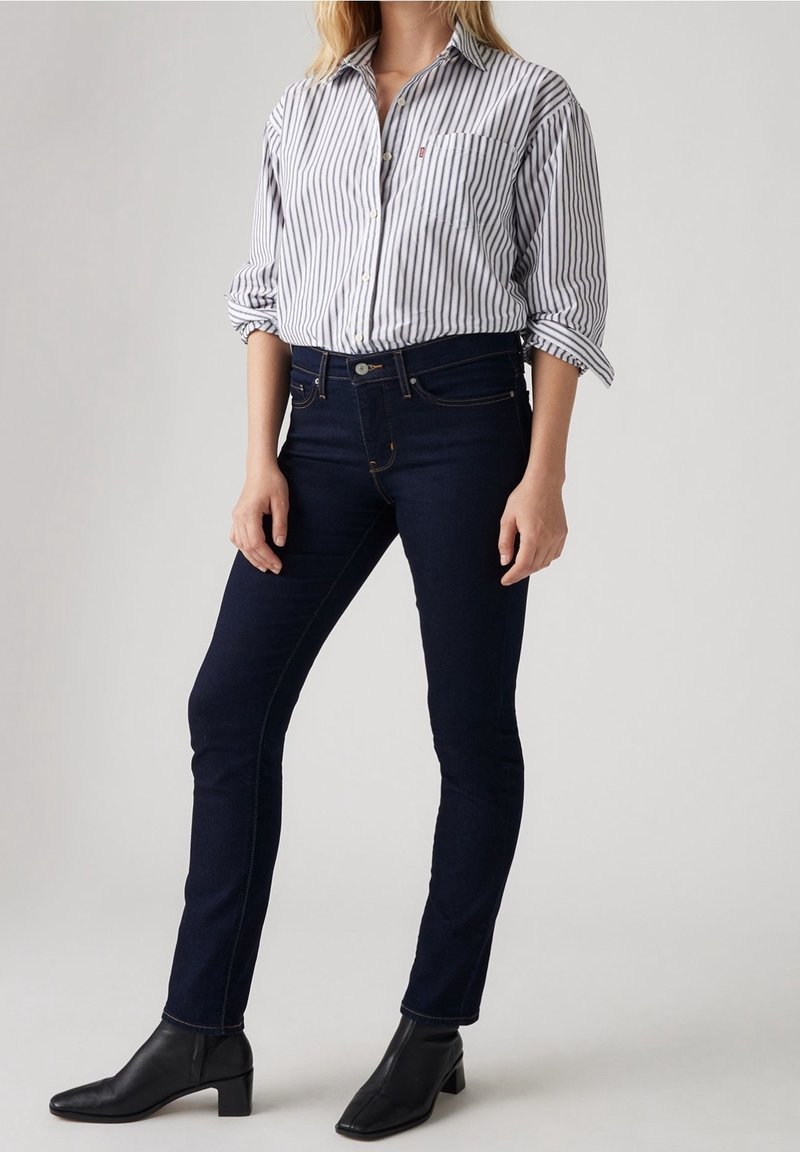 Chemise boutonnée à rayures verticales bleues et blanches, associée à un jean skinny bleu foncé et des bottines à talons noires.