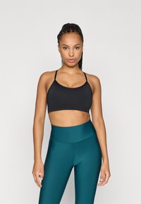 Μαύρο αθλητικό σουτιέν με λεπτές τιράντες, συνδυασμένο με ψηλόμεσες τυρκουάζ κολάν. Το ύφασμα φαίνεται λείο και ελαστικό. Απλός, λειτουργικός σχεδιασμός.