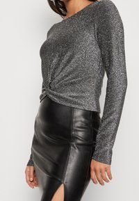 Grå glittrig långärmad topp med en snodd front, matchad med en åtsittande svart läderskjol med slit på sidan. Mjuk textur, smakfull design.