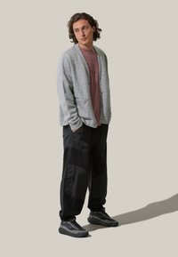 Cardigan grigio chiaro con una finitura testurizzata, indossato sopra una camicia color malva, abbinato a pantaloni neri sartoriali con un motivo geometrico. Sneakers scure completano il look.