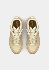 Beige Wanderschuhe mit strukturiertem Obermaterial, Gummisohlen und weißen Schnürsenkeln. Das Design umfasst ein weiches Innenfutter und ein Logo auf der Zunge.