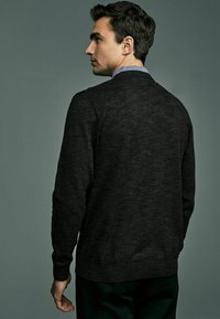 Pull en tricot gris foncé avec un col rond, des poignets et un ourlet côtelés. La texture est douce et légèrement texturée, avec un motif léger chiné.