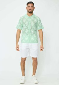 Polo mint, à manches courtes, avec un motif en diamant et un devant à boutons. Porté avec un short blanc et des baskets blanches.