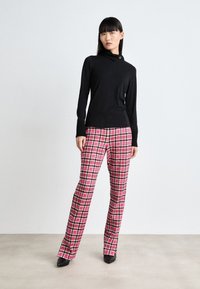 Haut noir à manches longues avec un col montant et des poignets côtelés, associé à un pantalon à carreaux rose et blanc, complété par des talons noirs pointus.