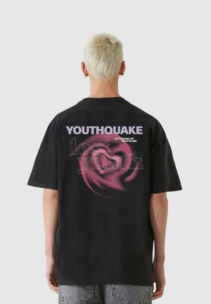 Sort bomulds T-shirt med korte ærmer. Ryggen har hvid og pink grafisk tekst: "YOUTHQUAKE," svungent mønster og "LAD OS RYSTE SYSTEMET."
