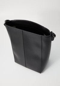 Svart läder tote-väska med en strukturerad design, slät textur och ett justerbart axelband. Den har vertikal panelering och minimalistisk branding.