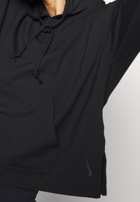 Schwarzer Hoodie mit einer frontalen Tasche, verstellbaren Kordeln und seitlichen Schlitzen. Hergestellt aus weichem Stoff mit einem dezenten Nike-Logo am Saum.