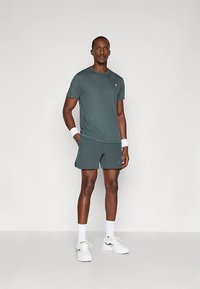 Roupa atlética masculina composta por uma t-shirt ajustada cinzento escuro e calções coordenados, feitos de tecido leve. Inclui pulsos brancos e sapatos.