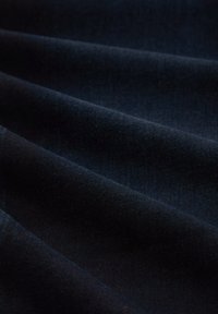 Gros plan sur un tissu bleu marine foncé avec des plis doux et une texture visible mettant en valeur le matériau tissé lisse.