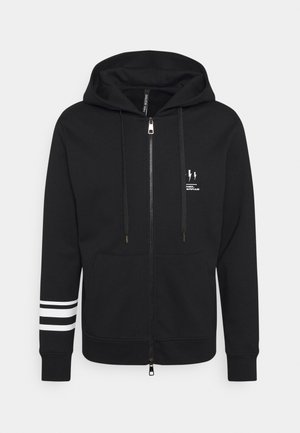 Sweat à capuche noir zippé avec poches avant, doubles bandes blanches sur la manche gauche, petit logo éclair blanc et texte sur la poitrine gauche.