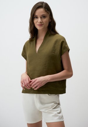 Olijfgroene linnen top met een v-hals, korte mouwen en een losse pasvorm, gecombineerd met witte shorts. De gestructureerde stof zorgt voor een casual uitstraling.