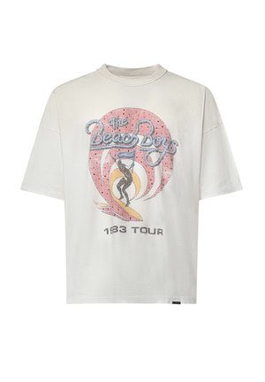 T-shirt bianca a maniche corte con testo "The Beach Boys", grafica vintage di una tavola da surf e "1983 Tour" stampato sotto il design.