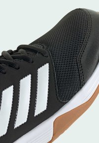 Black athletic shoe with a textured mesh upper, white three-stripe logo, and a brown rubber sole. Features black laces and contrasting stitching.