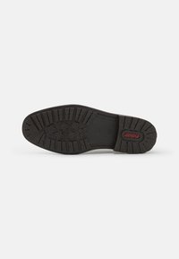 Suola di scarpa in gomma nera con motivo di grip testurizzato, caratterizzata da battistrada a forma di fiore e un logo centrale rosso, forma rettangolare con tacchi.