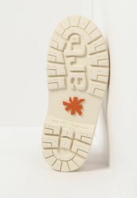 Suela de un zapato en goma blanco roto con surcos profundos, que presenta un logo de estrella naranja y el texto en relieve "THE ART COMPANY".