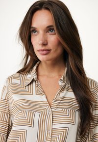 Camicia a fantasie con strisce geometriche in marrone e crema, realizzata in tessuto leggero, con chiusura a bottoni e un design di colletto classico.
