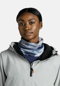 Gaiter de cuello multifuncional en tonos azules y grises con un patrón de montañas. Tela suave y elástica; usado bajo una chaqueta gris clara.
