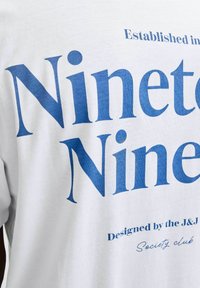 Tela blanca con gran texto azul que dice "Noventa y Nueve", texto más pequeño "Establecido en", y "Diseñado por el club J&J Society" en azul.