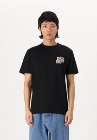 Schwarzes Baumwoll-T-Shirt mit Rundhalsausschnitt, das ein mehrfarbiges Grafik-Patch auf der linken Brust hat. Kurze Ärmel und lockere Passform.