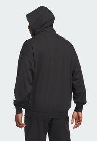 Schwarzer Kapuzenpullover mit entspannter Passform, ausgestattet mit einer weichen Stofftextur, gesenkten Schultern und gerippten Bündchen sowie Saum.