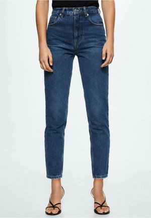 Dunkelblaue, hoch taillierte Denim-Jeans, zusammen mit schwarzen, mit Riemchen versehenen Sandaletten mit Absatz getragen, auf Knöchelhöhe gekürzt, an einer nach vorne gerichteten Person gezeigt.