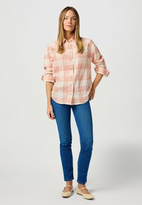 Camicia a maniche lunghe a quadri in pesca chiaro e crema, abbinata a jeans blu slim e ballerine beige. Presenta maniche arrotolate e tasche frontali.
