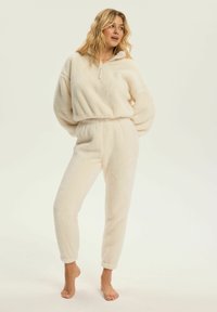 Zestaw loungewear w kolorze kremowym, składający się z krótkiej bluzki zapinanej na zamek oraz tapered spodni z elastycznymi mankietami, charakteryzujący się miękką, teksturowaną powierzchnią.