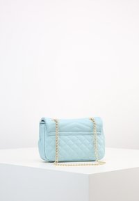 Ljusblå kviltad handväska med kedjesnodd. Har ett lock fram och en extra bakficka med slät textur och rena linjer.