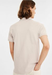 Licht beige poloshirt met korte mouwen, een zachte textuur en een klassieke kraag. Beschikt over een zijvent en een rechte zoom aan de achterkant.
