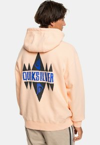 Sudadera con capucha de color melocotón que presenta un gran diseño gráfico en negro y azul con el texto "QUIKSILVER" en la parte posterior. Fabricada con un tejido suave y de corte relajado.