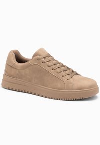 Beige mokkasiner av semsket skinn med flate lisser, rund tå, strukturert gummi såle og en glatt sideaccent. Rent design, minimal detaljer.