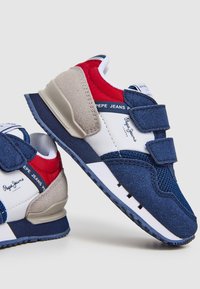 Tennarit tummansinisinä punaisilla ja vaaleanbeigeillä yksityiskohdilla, verkkokangasta yläosassa, tarranauhoilla ja tekstuurilla varustetulla kumipohjalla. Logo esillä sivussa.