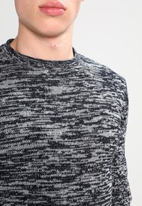 Maglione a maglia grigio e nero con collo a giro, che mostra un motivo testurizzato e una vestibilità rilassata, con un colletto a coste.