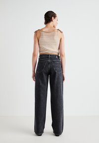 Stribet strik tanktop med bindebånd, parret med højtsiddende, løstsiddende sorte jeans med synlige baglommer og syninger.