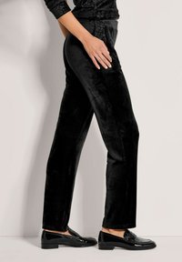 Schwarze Samthose mit geradem Schnitt und glatter Textur. Verfügt über ein Taillenbund-Design und wird mit glänzenden schwarzen Loafers kombiniert.