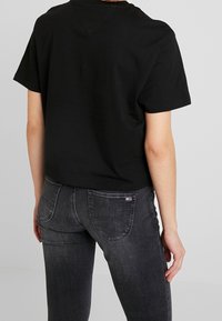 Černé zkrácené tričko s krátkým rukávem, vyrobené z bavlny, spárované s tmavě šedými skinny džíny s viditelným švem a zadními kapsami.