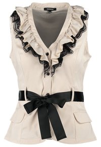 Blouse beige sans manches avec des volants en dentelle noire le long de l'encolure, fermeture par boutons, et une ceinture noire nouée à la taille.