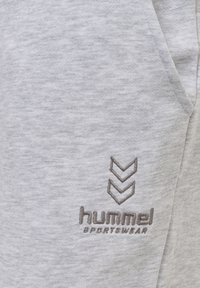 Tissu gris clair avec un petit logo Hummel Sportswear brodé en gris foncé près d'une poche latérale.